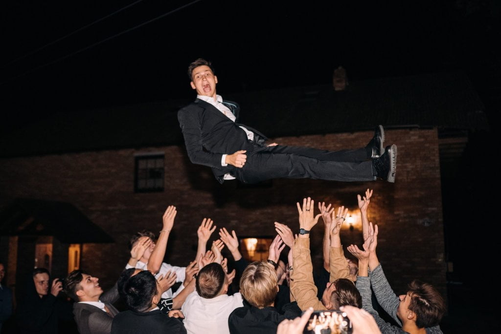 Groom being thrown in the air by group of friends at reception.