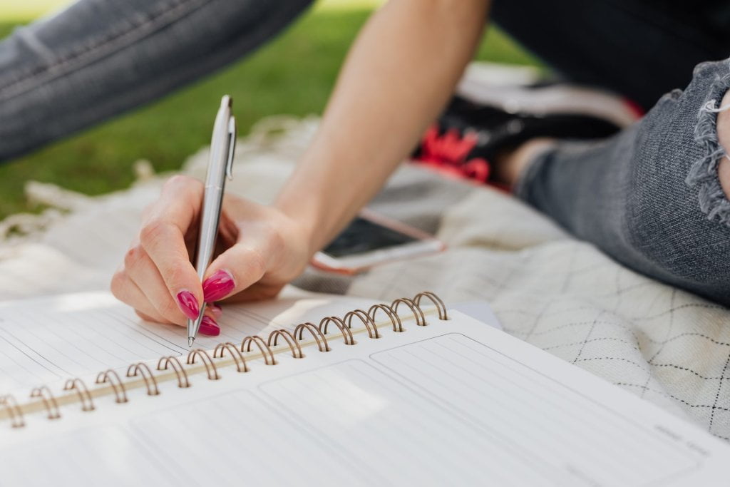 Woman sitting cross leg, writing in a planner.