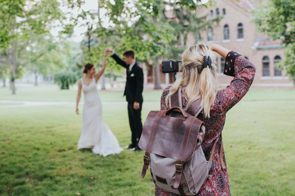 Wedding photographer in foreground taking photo of bride and groom in the background